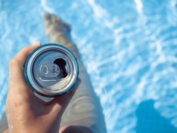 Can of beer and a cute woman on the background of the swim pool. Top view, close-up. Vacation and travel concept. Moments of celebration