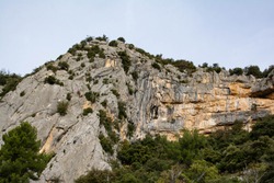 Climbers on a cliff in the south of France. Via Ferrata. Bushes, trees, a blue sky, grey and ocher colored rocks.