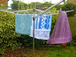 Washed towels blowing and drying in fresh air on garden rotary dryer on windy day 