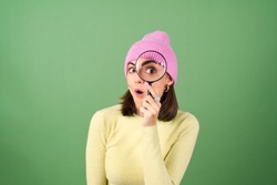 Young woman on green background in yellow sweater with magnifying glass