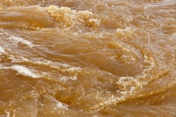 Muddy river water. Dirty muddy water with whirlpool and white foam close-up.