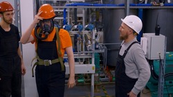 Three different male heavy industry engineers and uniformed workers stand in a petrochemical plant wearing a breathing mask. An industrial contractor uses a breathing mask in a gassed area