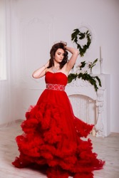 The beautiful girl in a long red dress posing in a vintage scene.Young beautiful woman wearing a red dress in the old hotel.Sensual elegant young woman in red dress and indoor shot.