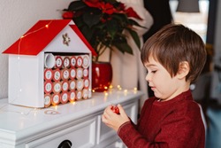 Little child taking chocolate opening first day in handmade advent calendar made from toilet paper rolls. Sustainable Christmas, upcycling, zero waste, kids seasonal activities 