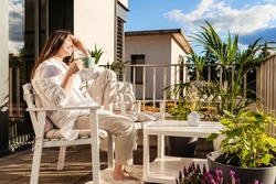 Beautiful young girl with long hair relaxing, drinking tea and enjoying sun sitting at balcony at sunlight at summer. Backyard terrace vacation.