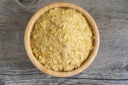 Nutritional yeast flakes in small bamboo bowl on textured wooden surface. Highly nutritious and healthy food, ideal for vegan recipes. Top center view with natural light.
