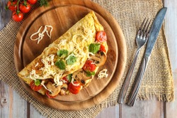 Omelet or scrambled eggs on a plate with grilled cherry tomatoes, grilled mushrooms, coriander and grated yellow cheese.  