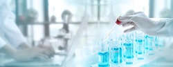 Test tubes with liquid in laboratory, Doctor hand holding dropper with dripping transparent glass pipette. scientist working with laptop background for banner size text space.