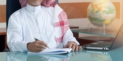Senior Saudi Businessman Hand Writing At His Desk with Laptop