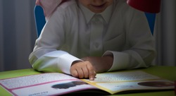 Saudi boy reading a story at a table with lamp close up