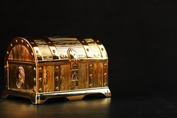Gold treasure chest on a black textured background. Closed box with money and jewelry. Free space