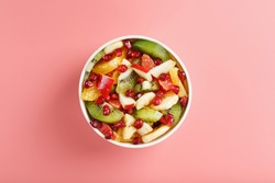 Bowl with fruit salad on a pink background. Juicy and ripe fruit slices. Top view
