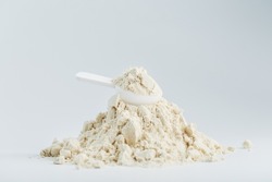 A mountain of soy protein isolate in powder with a measuring spoon on a white background. Vegetarian sports nutrition for cocktails