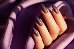Female hand with a long nails in grey color and purple shimmer on a violet silk textile background 