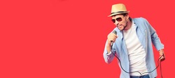 A Caucasian man in a hat and sunglasses sings a song into the microphone. Vocal performance of the song. Advertising banner for karaoke club or bar. Emotional singer. Studio portrait on a red