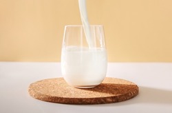 Pouring milk in glass on a light neutral background.