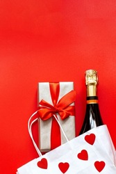 Valentine's Day background. Gift box, red hearts, bottle champagne, white paper bag on red background.Concept: Valentine's day, birthday. Flat lay, vertical.