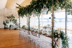 Banquet tables decorated with arrangements of flowers, herbs and candles in the tent. Wedding. Banquet.Crystal chandeliers hang from above