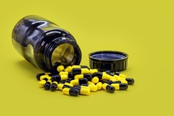 bottle of black and yellow pills on yellow background, caseia aor caffeine pills used in bodybuilding for muscle mass
