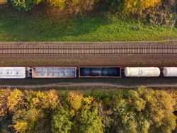 Aerial view of cargo train, a double-track railway in countryside. Railroad with green grass and fall trees with yellow foliage, top view. Transport infrastructure, train track, autumn nature