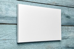 White canvas hanging on light blue wooden wall. Mockup, wall decor, blank canvas stretched on stretcher bar, side view