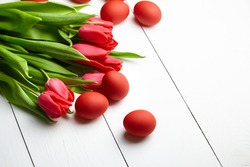 Easter Eggs and red flowers on white wooden table. Painted chicken eggs and red tulips, Easter Day decor, selective focus