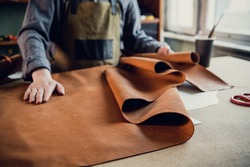 A young apprentice in a boot workshop prepares leather for further use on a large table