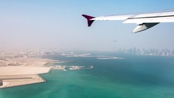 View of the city of Doha, Qatar from the airplane porthole. Plane flies over the skyscrapers. Travel concept.