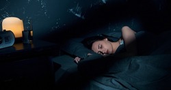 Beautiful young brunette woman sleeping on side, lying cozily in bed, hugging a pillow. Lady sound asleep at night. Loft interior.