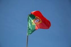 View of a flag of Portugal on a flagpole waving in the wind, blue sky background...