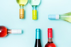 Layout frame of foil caps in different bright colors of white and rose wine bottles on blue background with copy space. Minimal abstract colorful mockup concept of alcohol beverage. Flat lay. 
