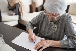 High angle view of a senior Caucasian woman doing Alzheimer's disease cognitive functions clock drawing self assessment test at home with positive results suggesting illness
