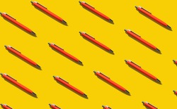 Bright orange repeating pens on a yellow background. Concept for learning, literature, writing texts