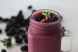 Mixed berry smoothie. Thick and creamy smoothie made of fresh strawberry and mulberry in almond milk. Served in smoothie jar. Shot on white background along with mulberries around