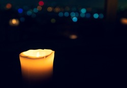 Close up pantone backround image of candle and its flame with window on the background and big city refletions.