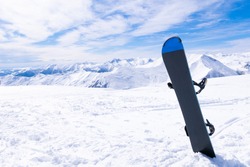 Black/blue snowboard in a snow with white mountains in the background. Concept of end of ski season.Gudauri. Sakartvelo. Georgia. 2020
