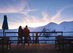 Gudauri, Georgia - 14th february, 2022: Couple together sit enjoy sunset in winter ski resort with snowy peaks background. Valentines day in winter concept. Togetherness connection concept