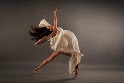 Young pregnant ballerina performing classical ballet pose with silk cloth in studio