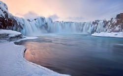 Godafoss frozen waterfall during Winter at sunrise. North Iceland.