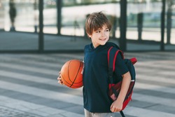 Portrait of a beautiful boy in sports uniform with a backpack and a basketball. The boy smiles and holds the ball in his hands. Training, education