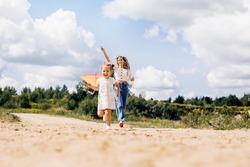 A laughing little girl and her mother run along the road to the field and fly a kite. Mom and daughter have fun together