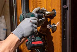 The master worker installs a door lock in the front door, metal doors with a polymer coating.