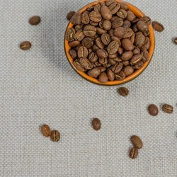 Cup with coffee beans on the background, spilled coffee beans near the cup, top view of coffee.