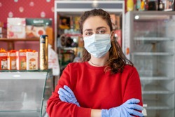 A woman in a medical mask and rubber gloves, posing with her arms crossed. In the background-shelves and shop Windows. The concept of coronovirus, quarantine and crisis in business