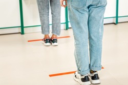 People stand in line, legs close-up. Attention line on the floor of the store to maintain social distance. Concept of the coronavirus pandemic and prevention measures