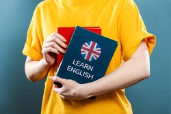 English Language Day. A woman holds English textbooks in her hands. Close-up of books. Blue background. The concept of learning foreign languages.