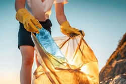 Earth day. A female activist puts a plastic bottle in a garbage bag. Close-up. The concept of environmental conservation and coastal zone cleaning.