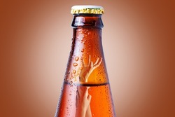 Close-up of the neck of a wet glass bottle of dark beer on a brown background. Inside it drowning hand. The concept of alcoholism and alcohol dependence.