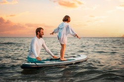Surfing with sup board. Instructor teaches the pre-school girl to swim with a sup board. Sea and the sunset in the background. Summer vacations.
