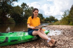 A young woman is sitting on a kayak, holding a paper map and check the route. Copy space. The concept of the World Tourism Day.